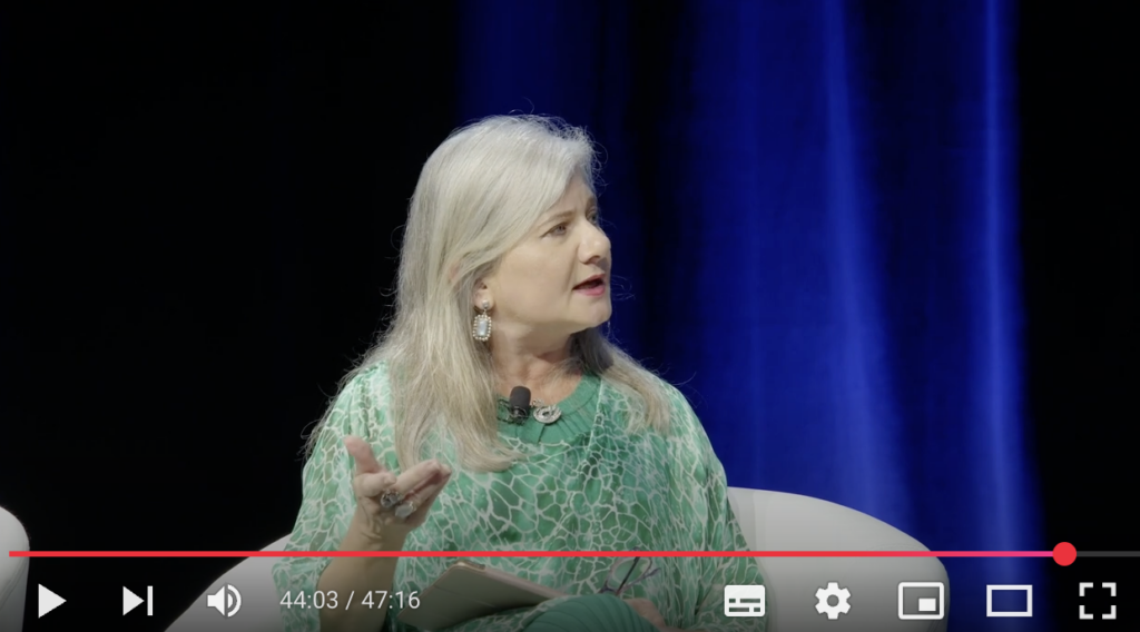 Image of Penny Jane Burke at the Universities Australia forum. Penny is speaking in conversation following her address. She is wearing green and is sitting in front of a blue background.